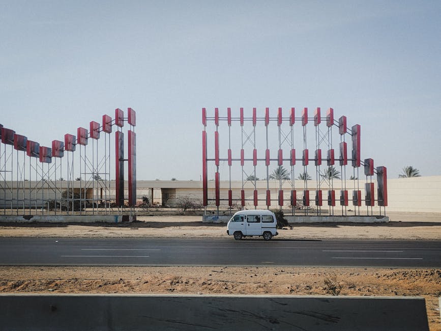 Van driving on desert highway between large metal billboards under clear sky.